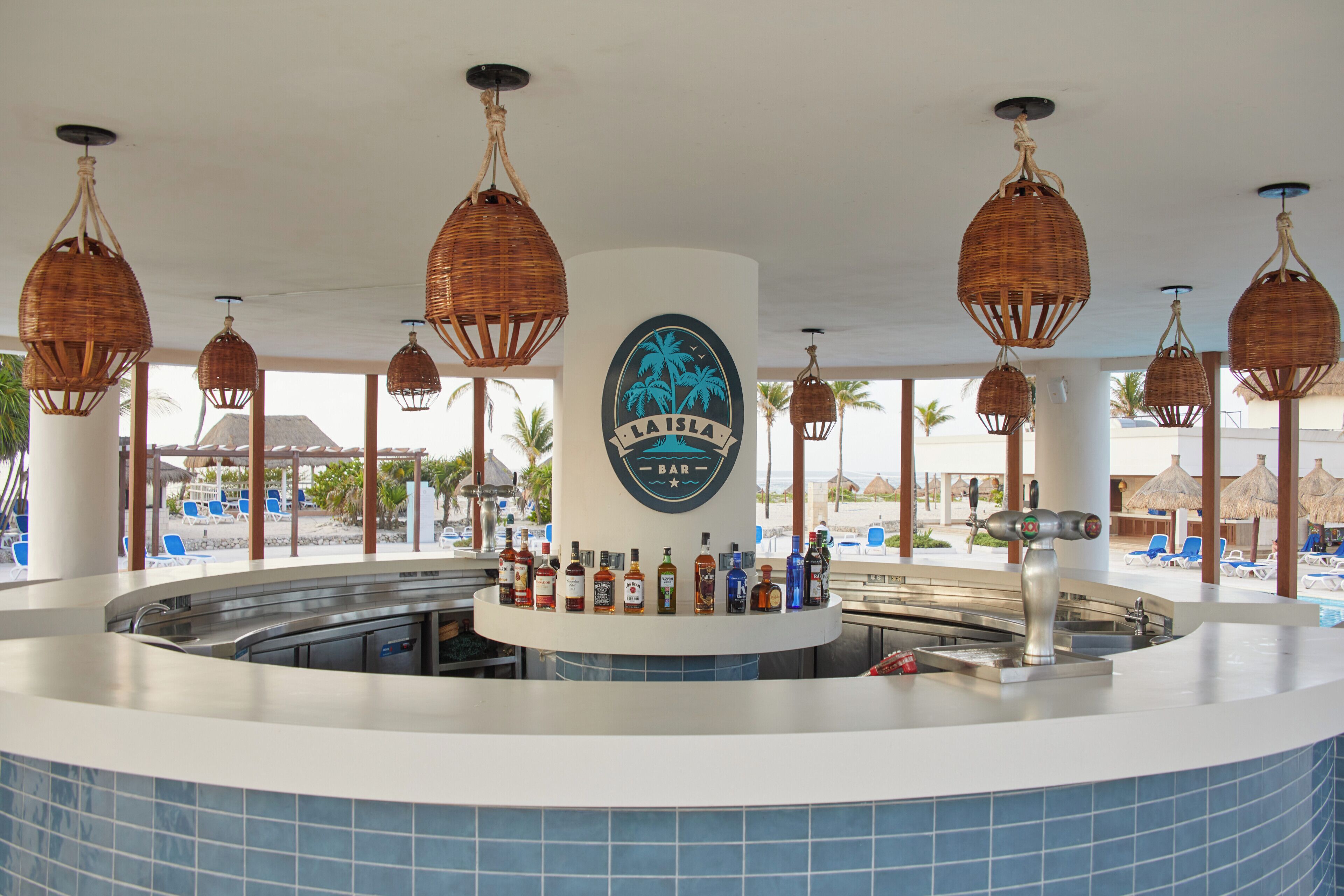 A bar area with a circular counter, a logo with palm trees, and hanging wicker lamps.