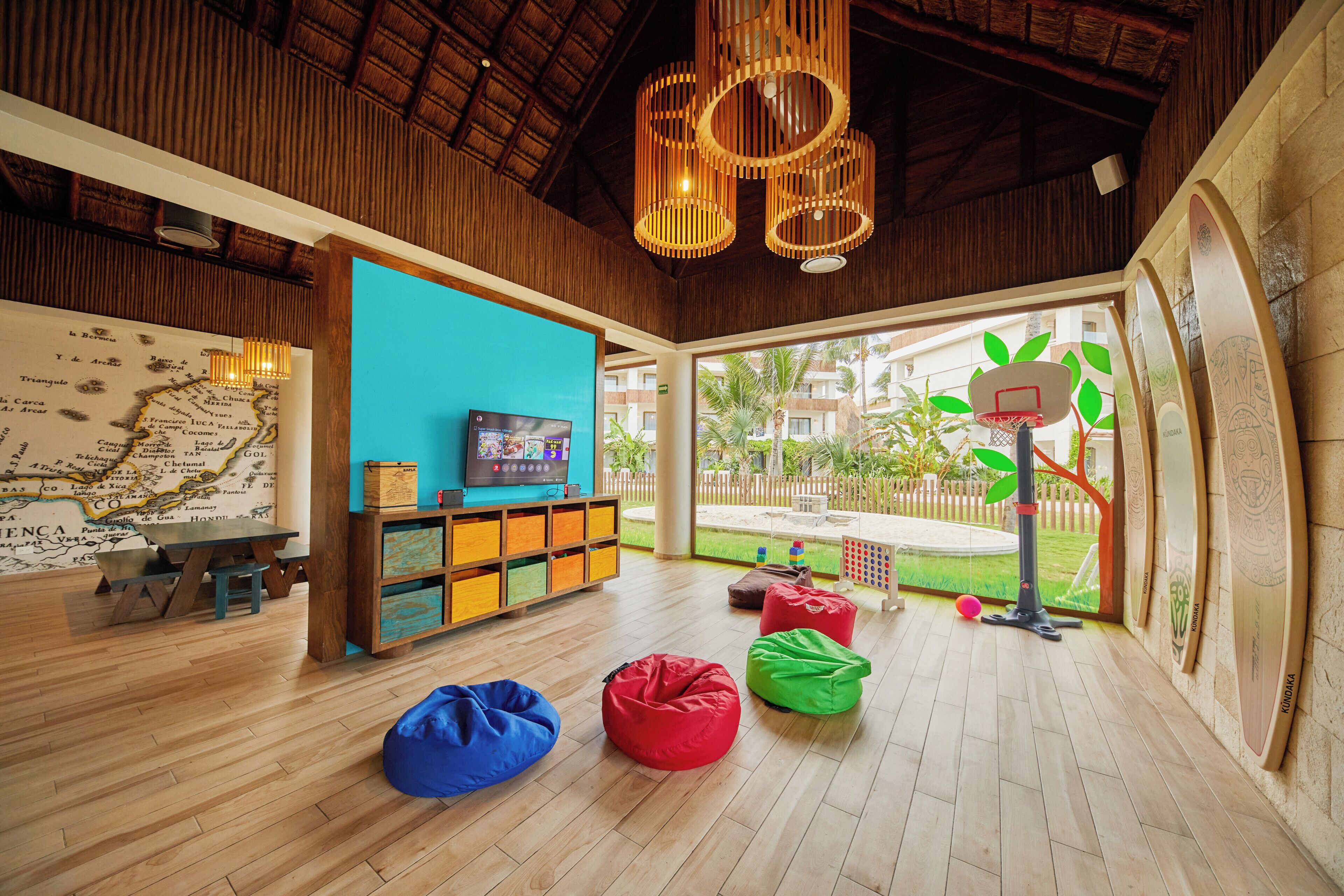 Une pièce avec un plafond en bois, une carte accrochée au mur, un téléviseur, des meubles de rangement colorés et des fauteuils en forme de sac.