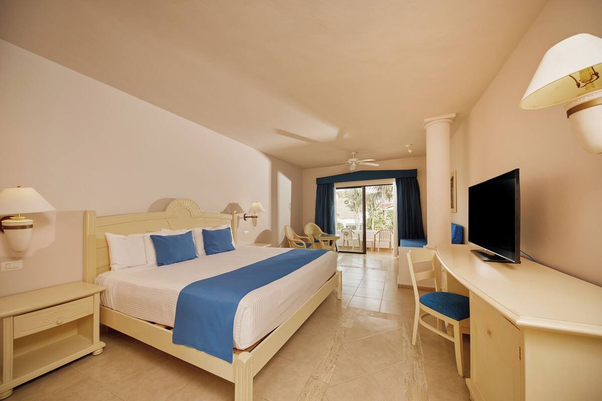 Une chambre d’hôtel avec un lit, un bureau, une télévision et un balcon équipé de chaises.
