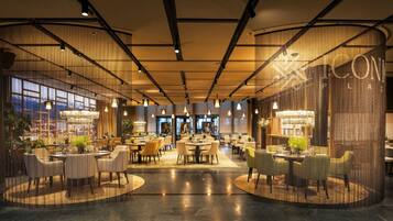 A spacious hotel lobby with multiple seating areas, large windows, and a modern chandelier.