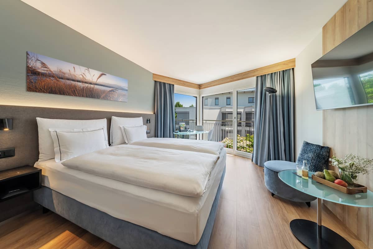 Una habitación de hotel moderna con una cama grande, un escritorio y un balcón con vistas a edificios.