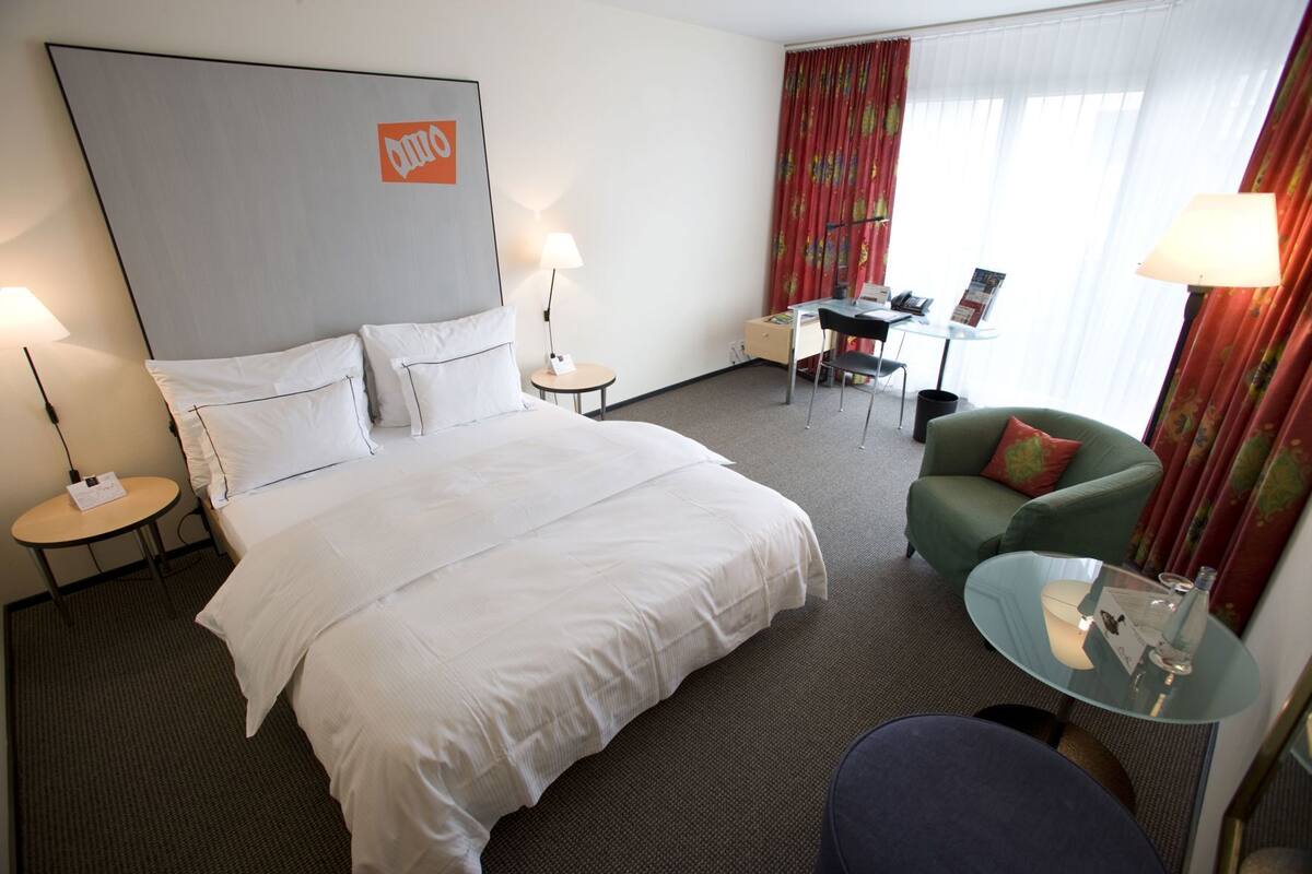 Una habitación de hotel con una cama grande, un escritorio, una silla, una mesita y un sofá.