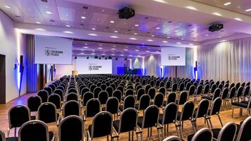 A conference room with rows of chairs, a stage, and large screens displaying the SEEDAMM PLAZA logo.