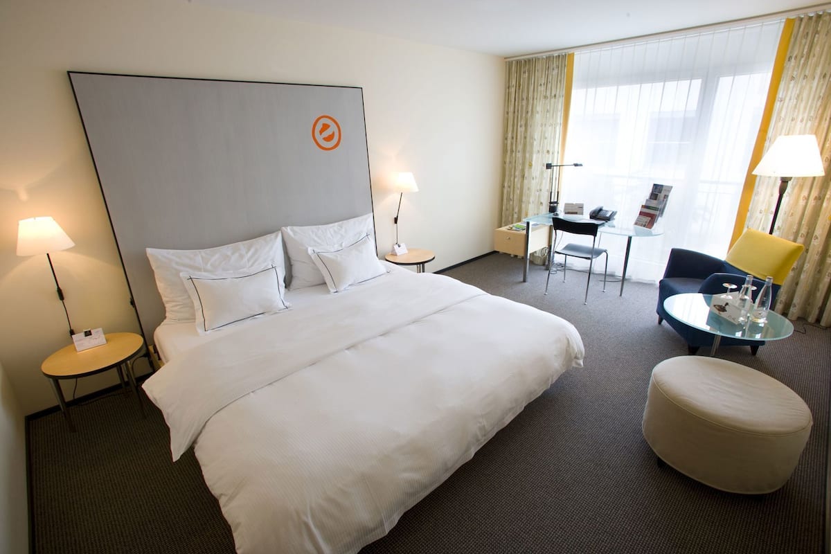 Habitación de hotel con una cama grande, dos mesitas de noche, un escritorio con silla, una pequeña mesa redonda con una silla y un sofá.