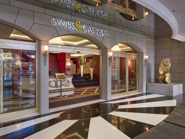 Entrada de SWISS CASINOS con un gran arco, un mostrador de recepción y un interior lujoso visible a través de las puertas de cristal.