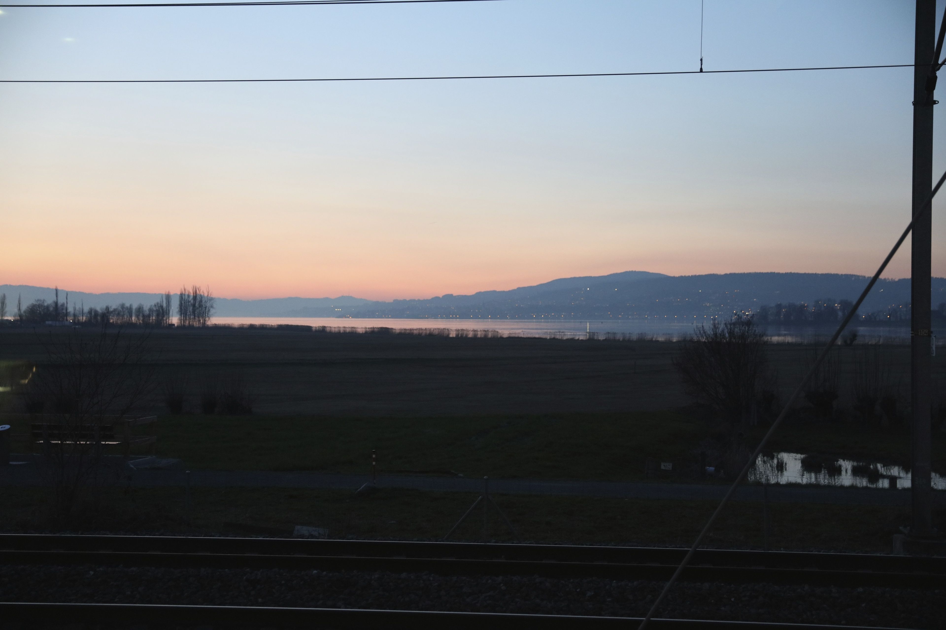 A view of a landscape with fields, a body of water, and distant hills.