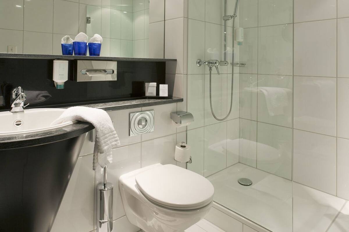 Un baño moderno con cabina de ducha de vidrio, una bañera negra y un inodoro blanco.