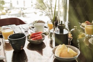 A breakfast table with various fruits, a coffee pot, and a glass of orange juice.