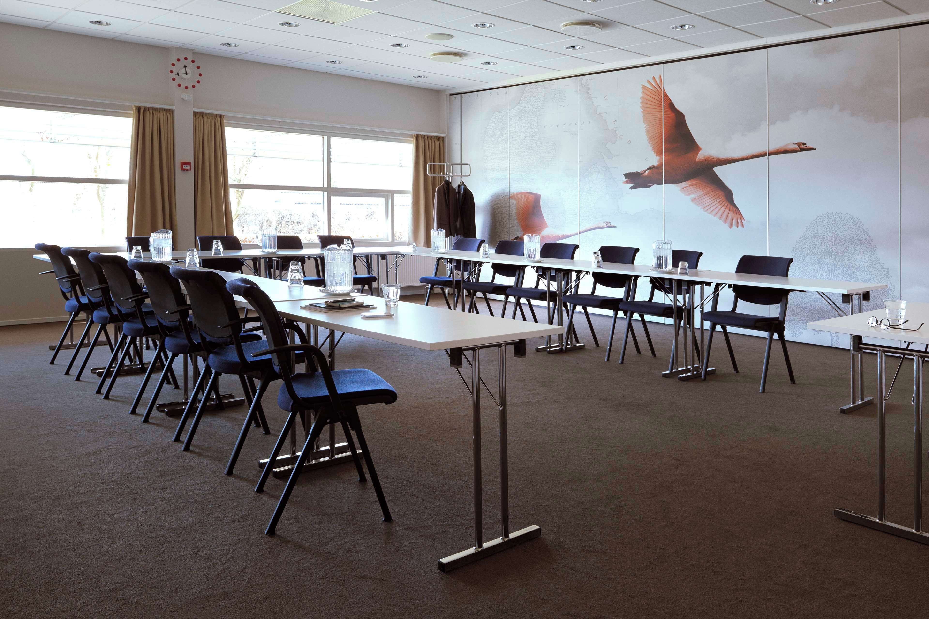 Un salón de conferencias con una larga mesa, sillas y un gran mural de un ave en vuelo.