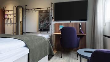 A hotel room with a bed, a desk, a chair, a TV, and a map on the wall.