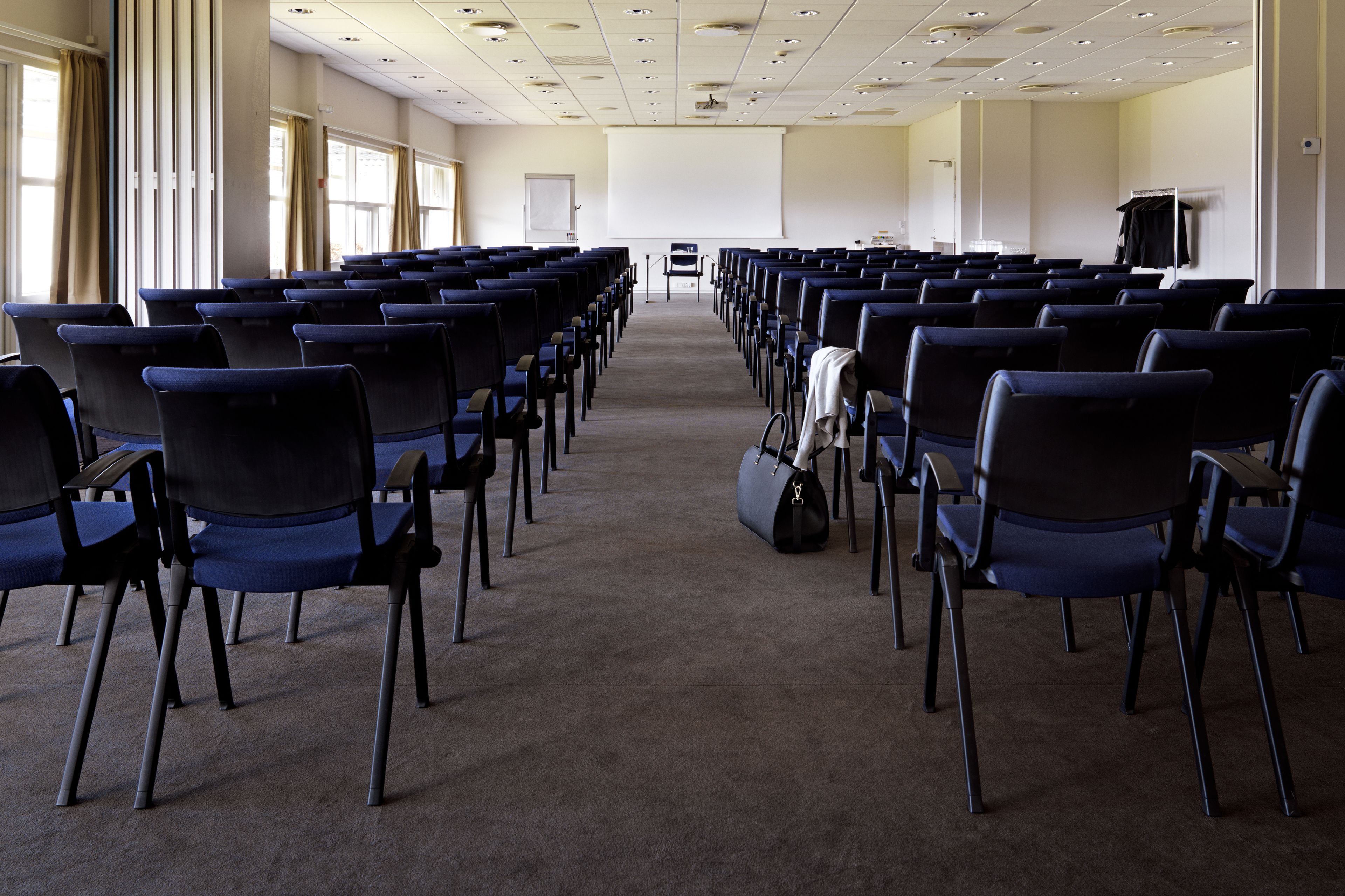 Ein Konferenzraum mit Reihen von Stühlen, einer Projektionsleinwand und einem Teppichboden.