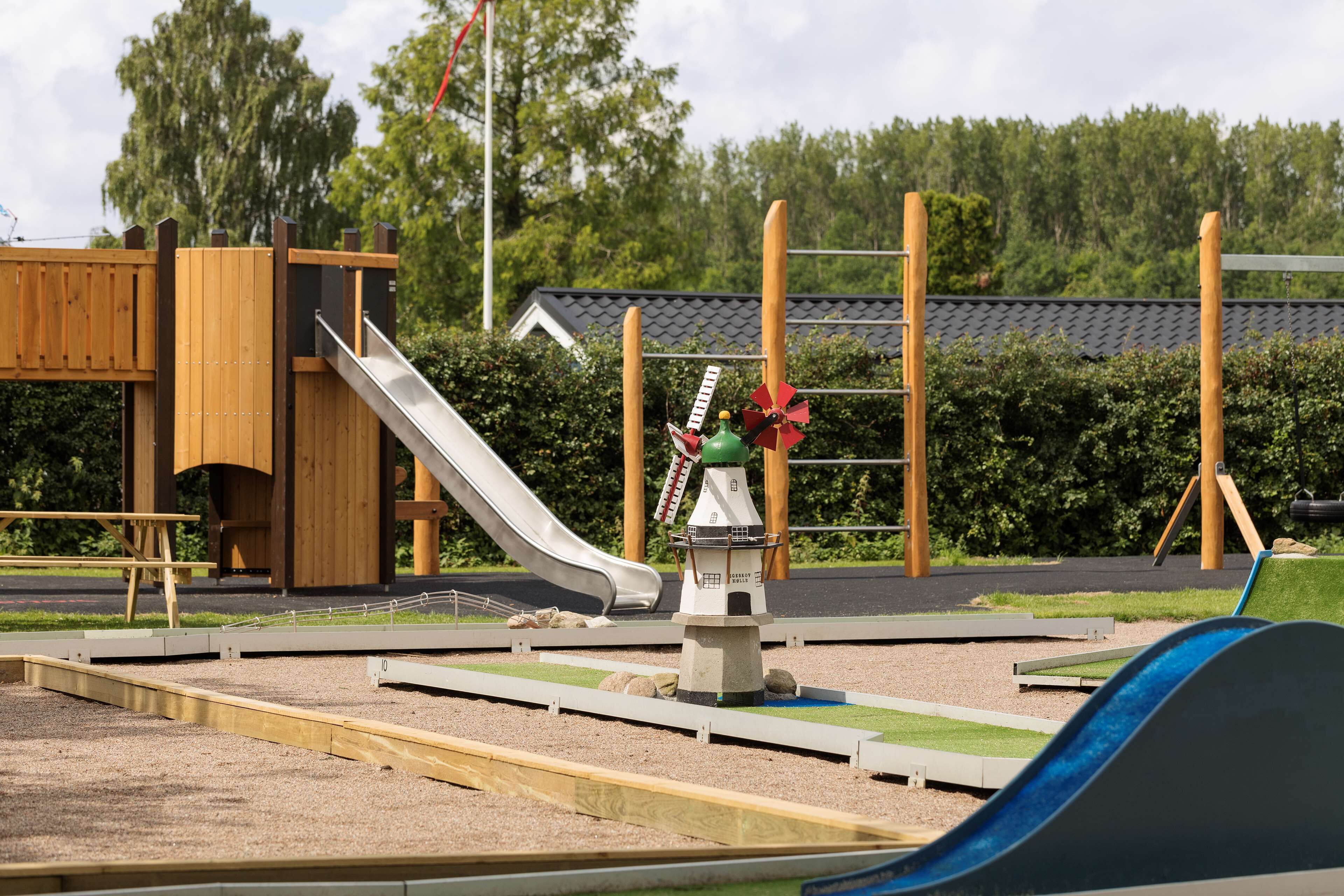 A playground with a slide, climbing structures, and a small building with a flag.