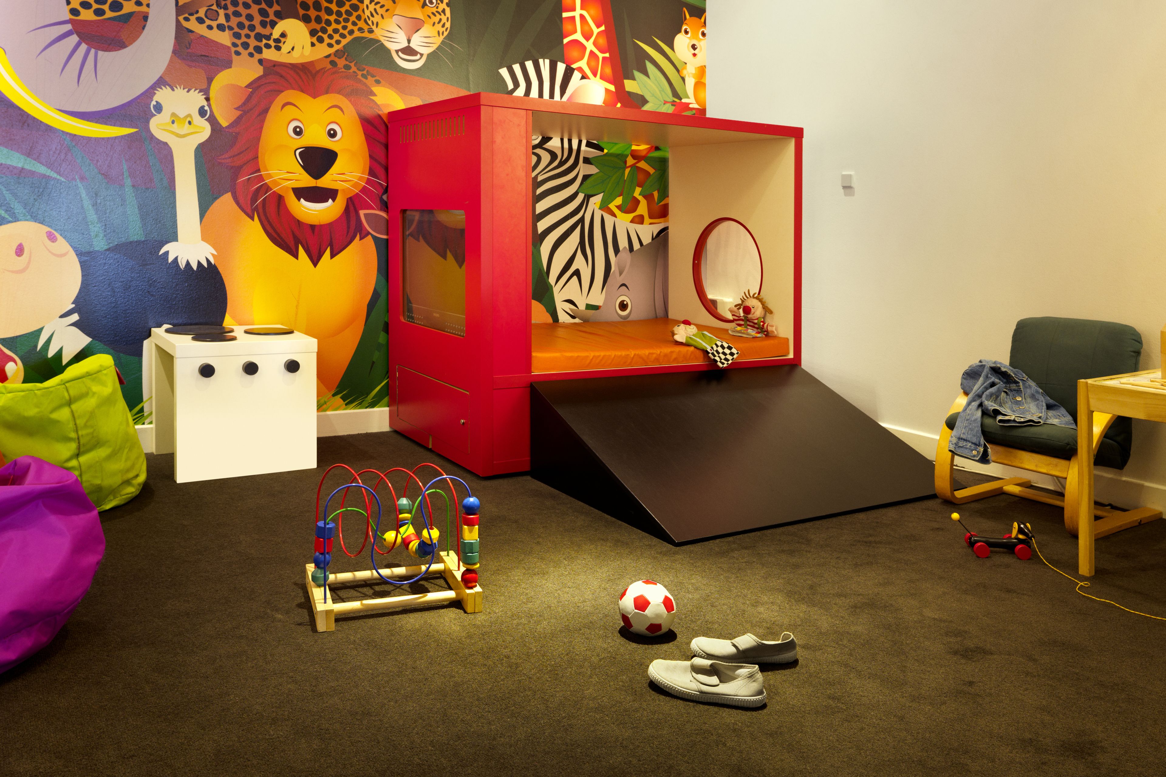 Una sala de juegos infantil con una casita roja, un aro de baloncesto, una pelota de fútbol y un coche de juguete.