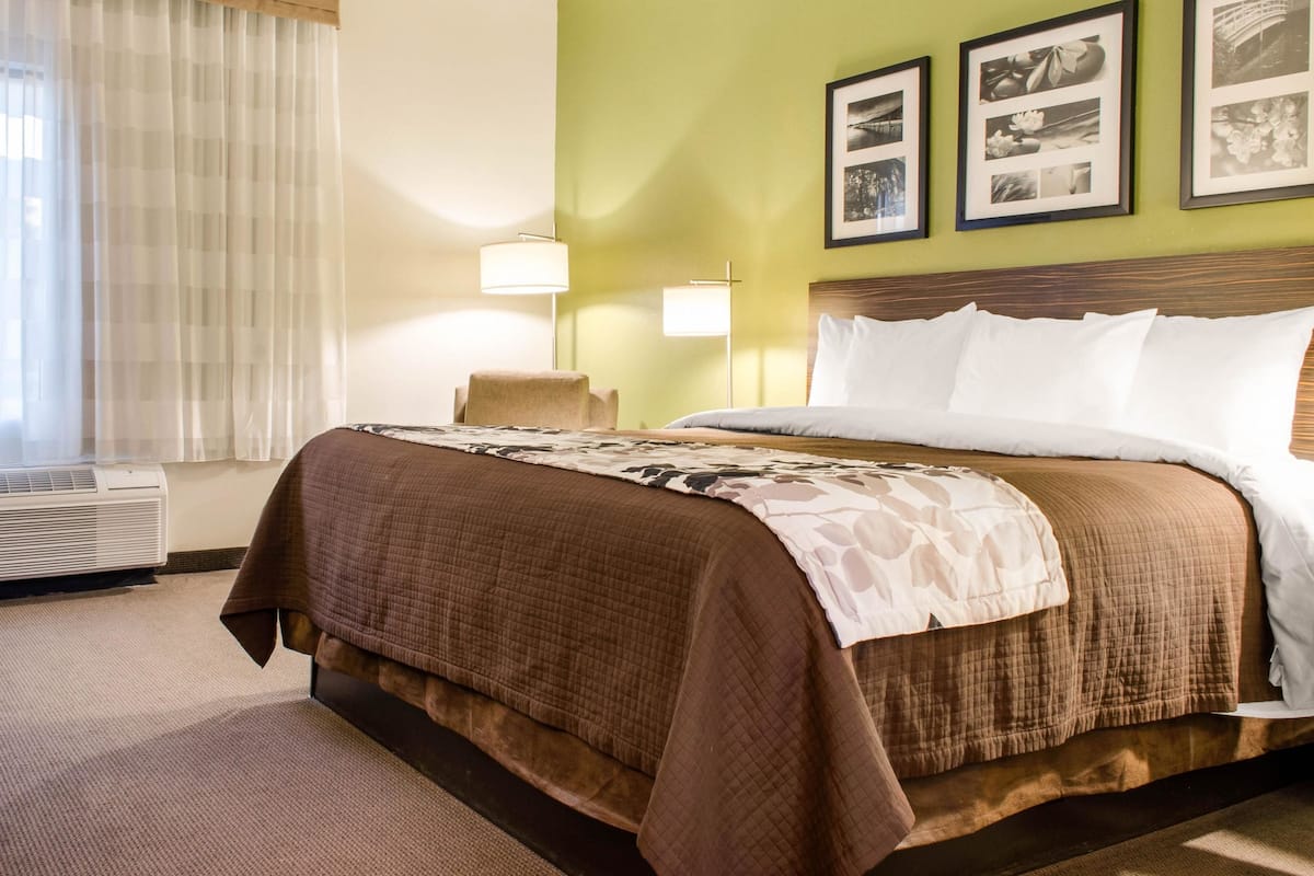 A hotel room with a large bed, a chair, a desk, and a wall with framed pictures.