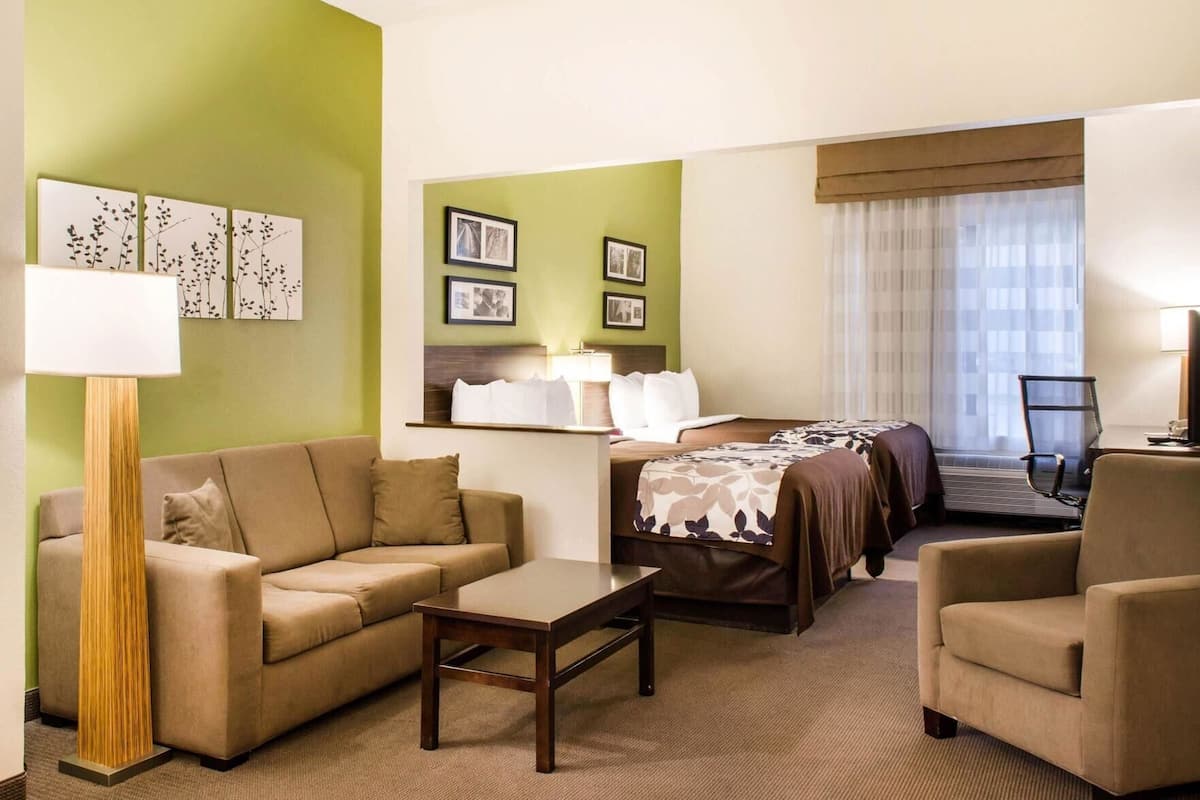 A hotel room with a sofa, a small table, a bed with a canopy, a chair, and framed pictures on the wall.