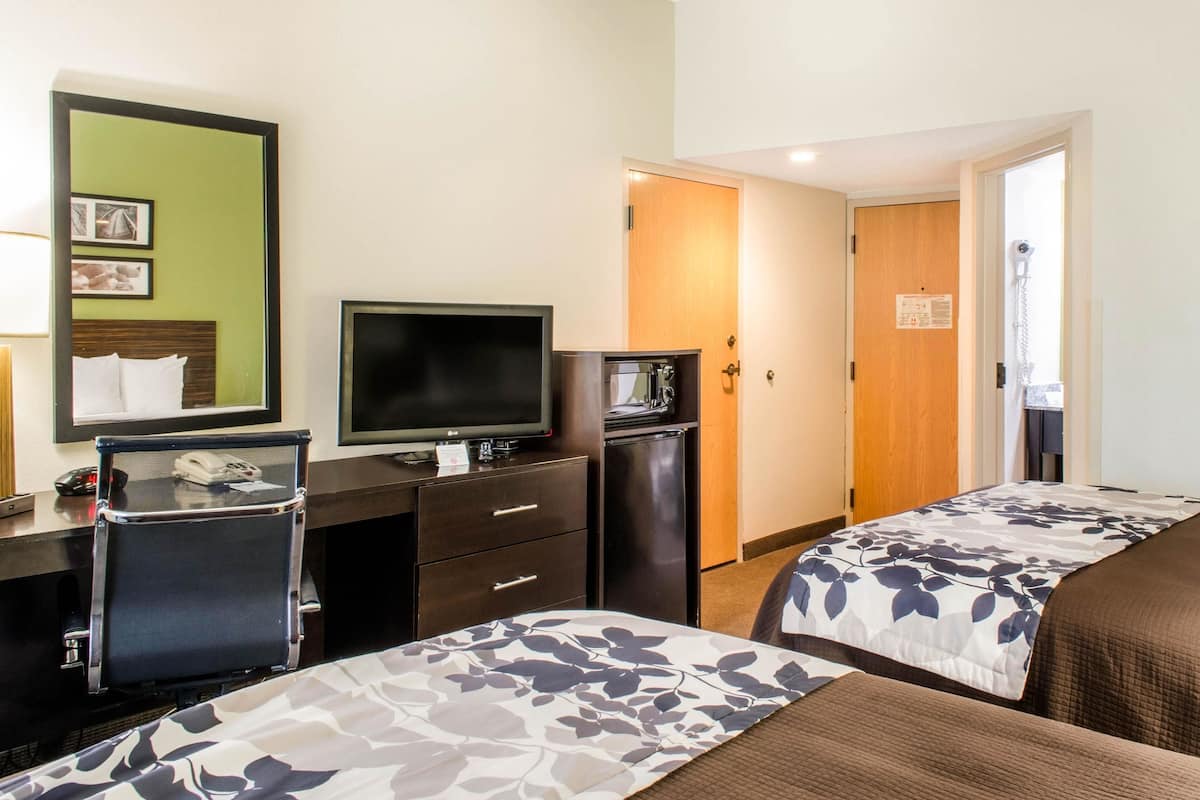 A hotel room with two beds, a desk with a computer and phone, a television, and a small refrigerator.