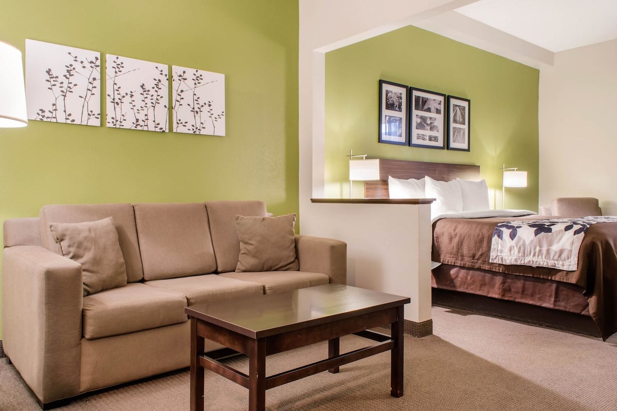 A room with a beige sofa, a wooden coffee table, a bed with a brown bedspread, and green walls.