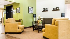 Eine Hotelhalle mit grüner Wand, einer Couch, zwei Sesseln, einem Couchtisch mit Blumen und gerahmten Bildern an der Wand.