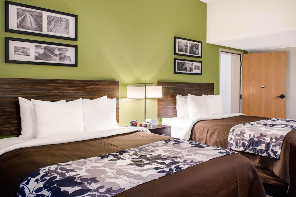 A hotel room with two beds, a nightstand, a lamp, and framed pictures on the wall.