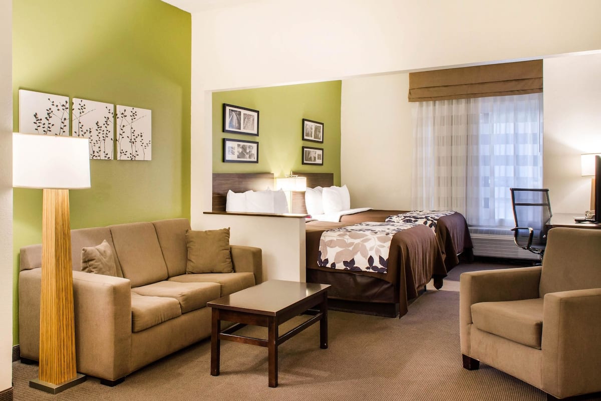 A hotel room with a green accent wall, a sofa, a bed with a floral bedspread, a desk, and a chair.