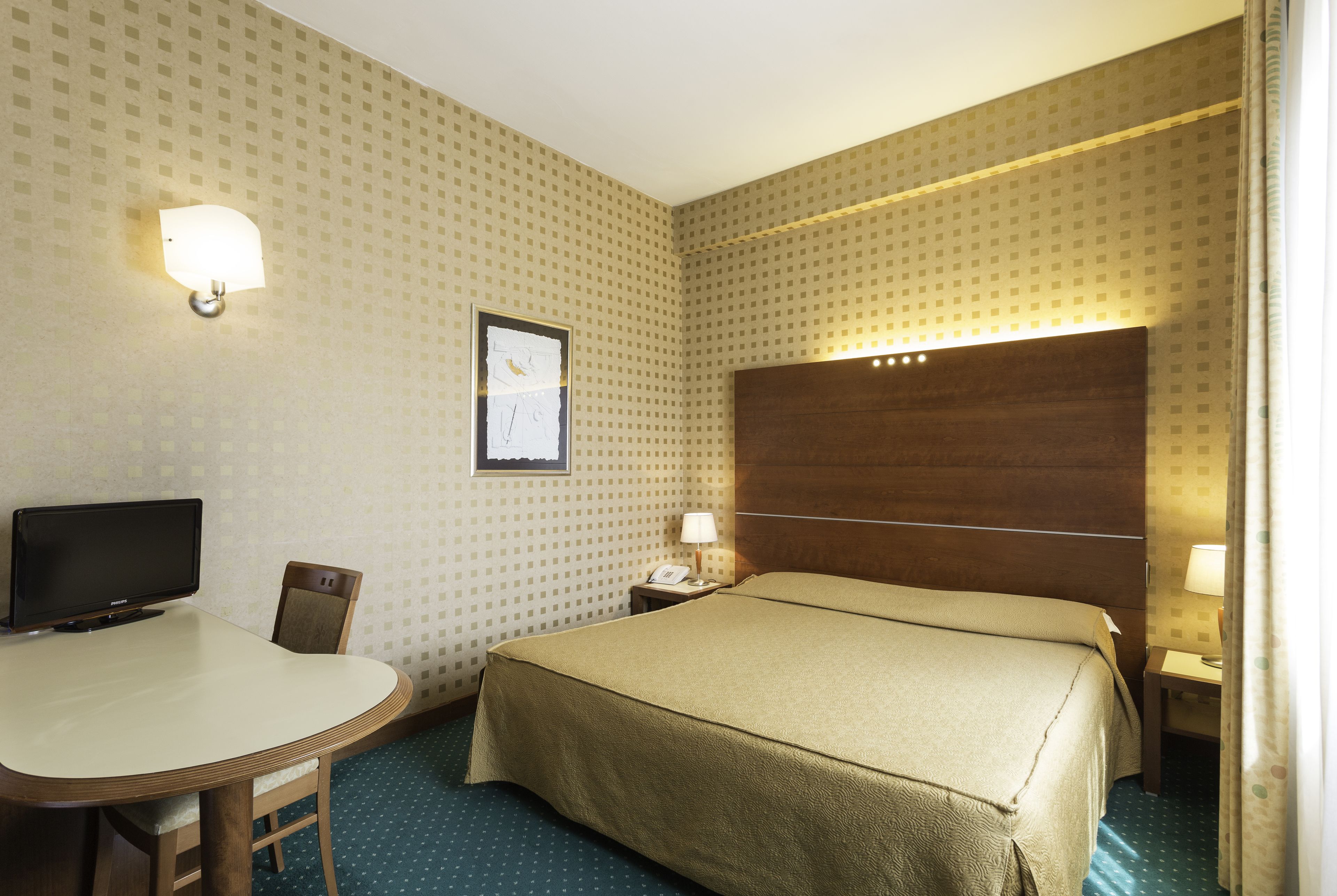Une chambre d’hôtel équipée d’un lit, d’un bureau, d’une chaise, d’une télévision et d’une table de chevet avec une lampe.