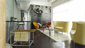 Un hall d’entrée moderne avec une table basse en verre, des chaises jaunes, un chariot en métal et une fresque murale.