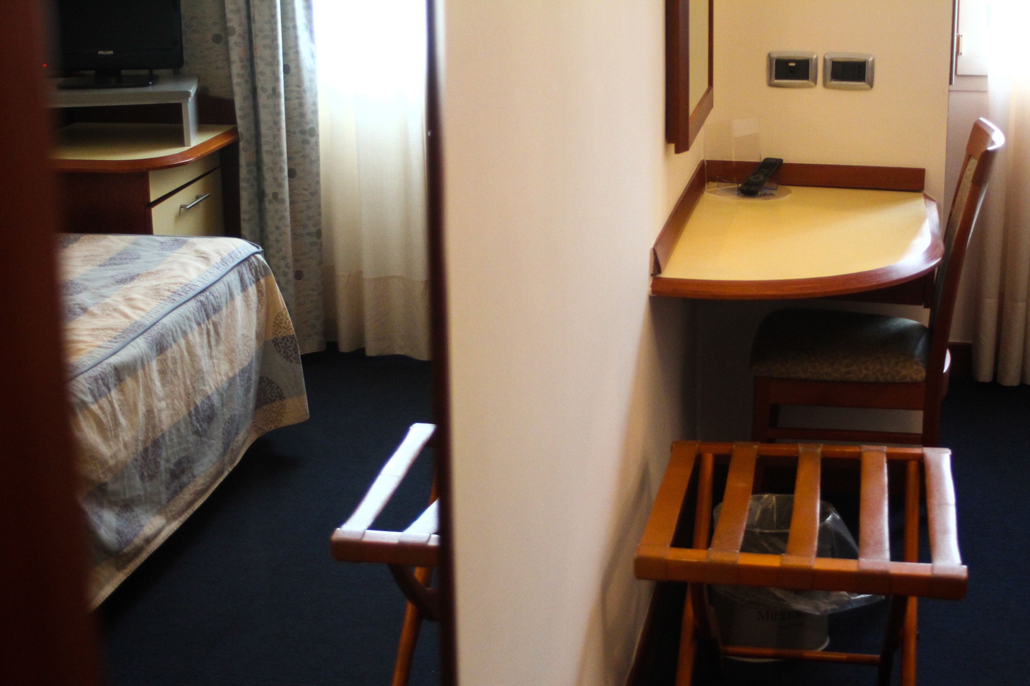 A hotel room with a bed, a desk, a chair, and a television.