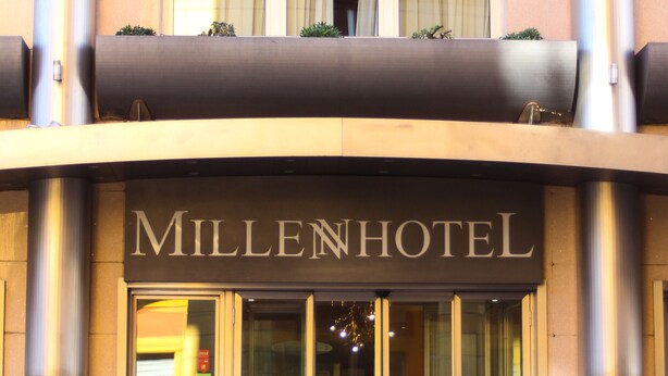L’extérieur du Millenhotel se distingue par son logo « M » bien visible, sa grande entrée vitrée et les plantes en pot qui l’ornent.