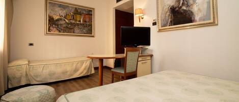 A hotel room with a bed, a desk with a chair, a television, and two paintings on the walls.