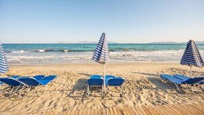 Ein Strand mit blauen Liegestühlen und gestreiften Sonnenschirmen.