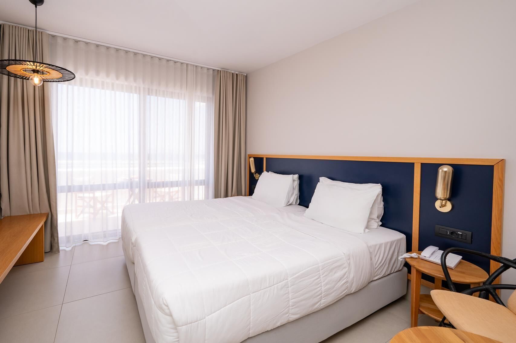 Habitación de hotel con una cama grande, un escritorio, una silla, un teléfono y una lámpara fijada a la pared.