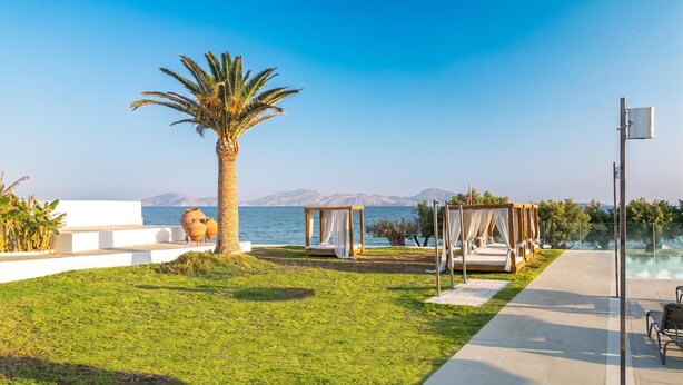 Ein Strandgrundstück mit Pool, einer Palme, einem Pavillon und einem weißen Gebäude.