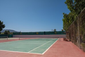 Un campo da tennis con una rete, circondato da una recinzione, e una panchina nei pressi della recinzione.