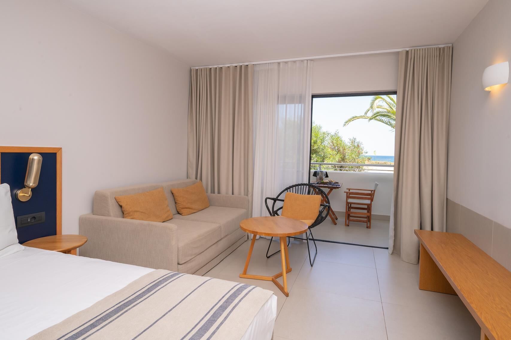 Una habitación de hotel con cama, sofá, mesita, silla y balcón con vistas.