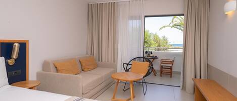 Una habitación de hotel con cama, sofá, mesita, silla y balcón con vistas.