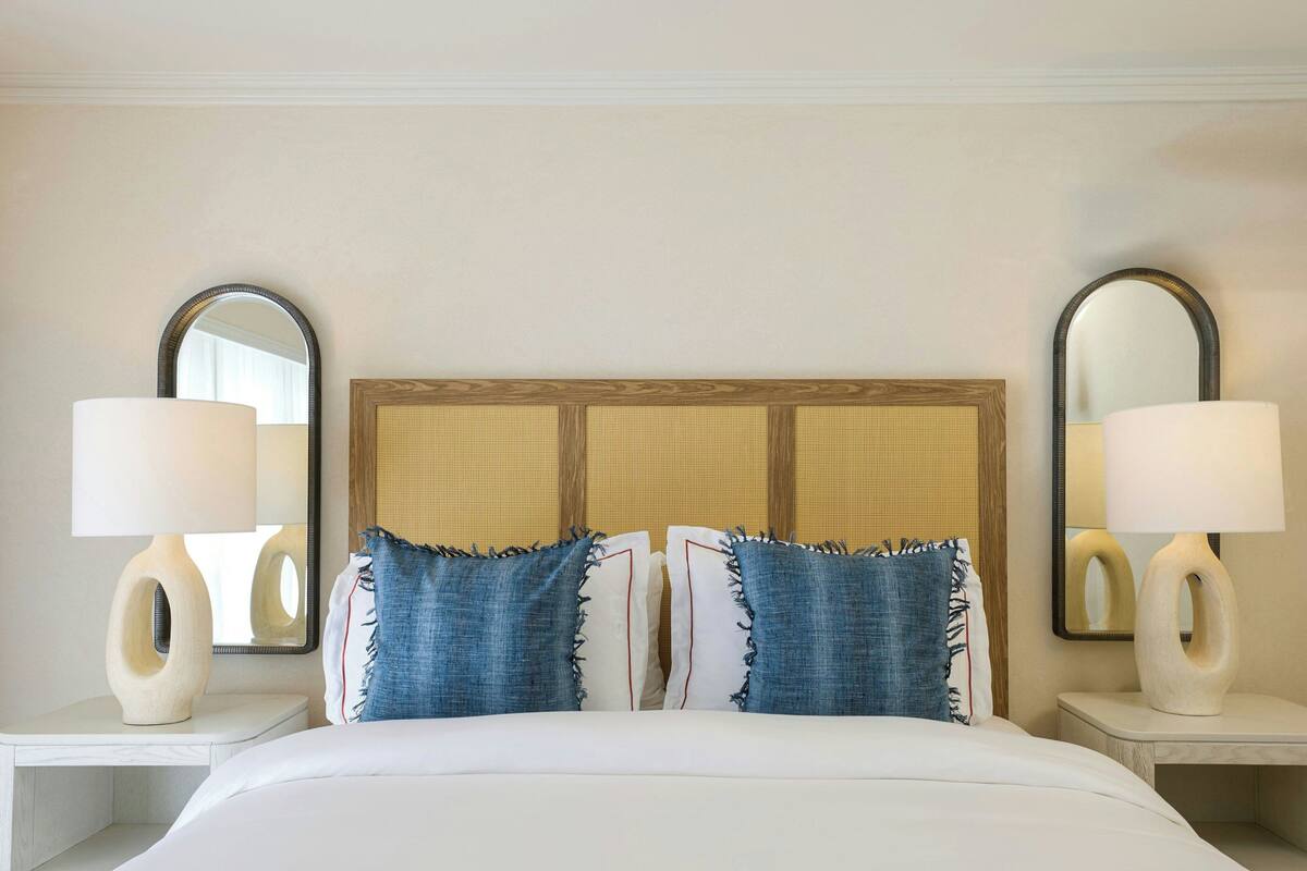 A hotel room with a large bed, two bedside tables with lamps, and two wall-mounted mirrors.