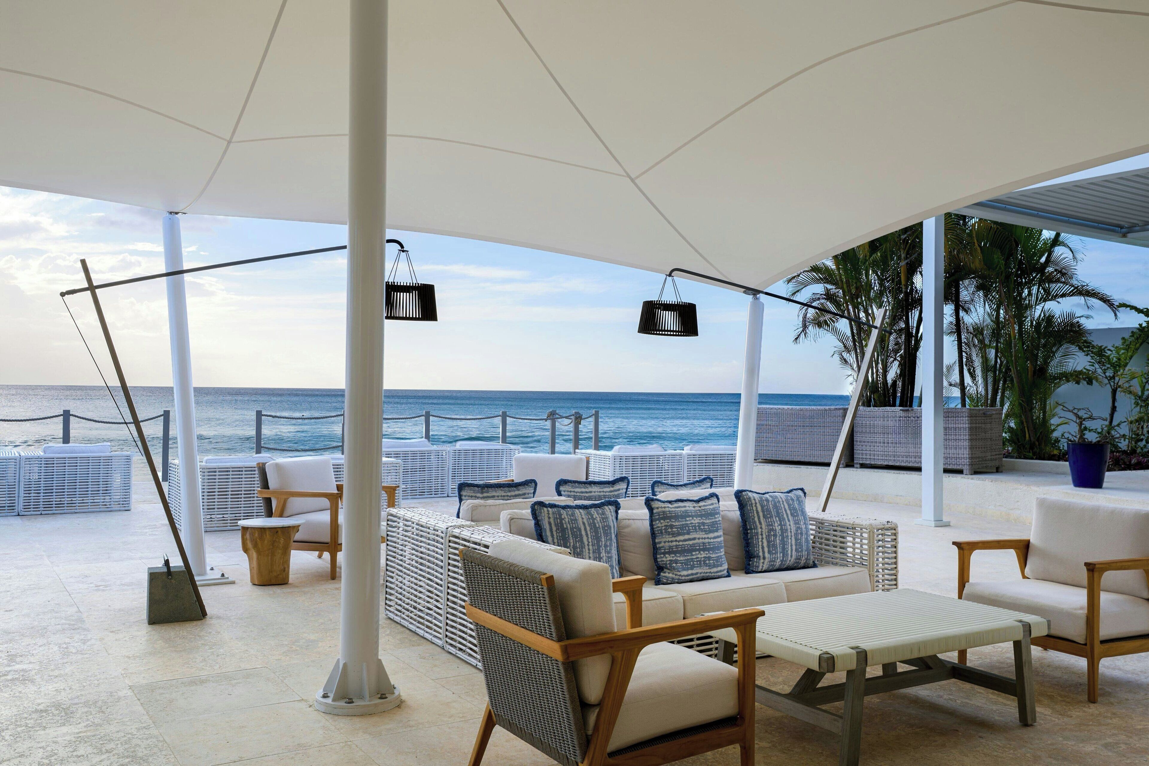 Un espace extérieur aménagé avec des meubles blancs, un grand parasol et une vue sur l’océan.