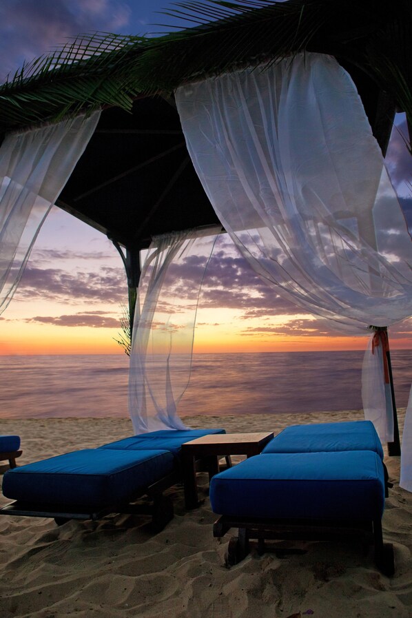 A beachside lounge with two blue cushioned chairs under a canopy.