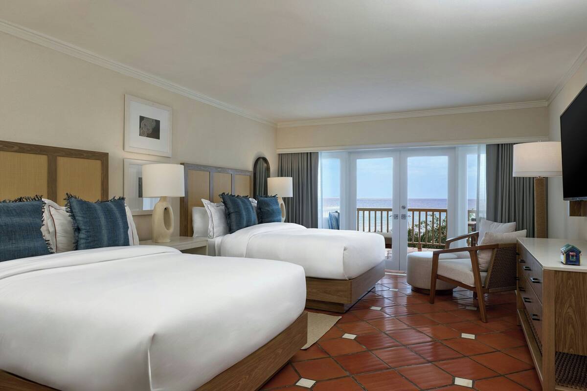 A hotel room with two beds, a desk, a chair, and a TV.