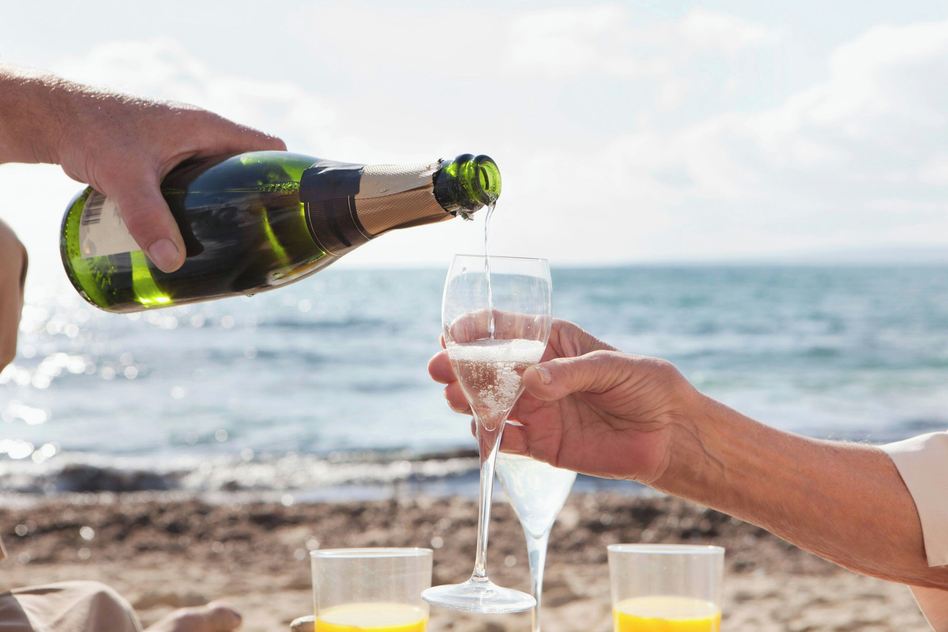 A person pouring champagne into a glass on a beach.