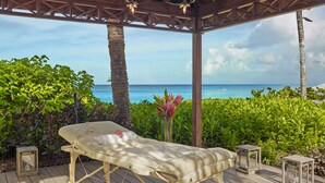 A wooden deck with a massage table, surrounded by lush greenery and overlooking a beach. - The House, An Autograph Collection All-Inclusive Resort - Adults Only (Paynes Bay)