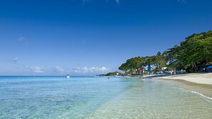 A beach with clear water, a boat, and beach umbrellas. - The House, An Autograph Collection All-Inclusive Resort - Adults Only (Paynes Bay)