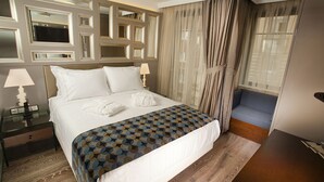 Une chambre d’hôtel avec un grand lit, une table de chevet avec des lampes, un canapé bleu et un grand miroir au mur.