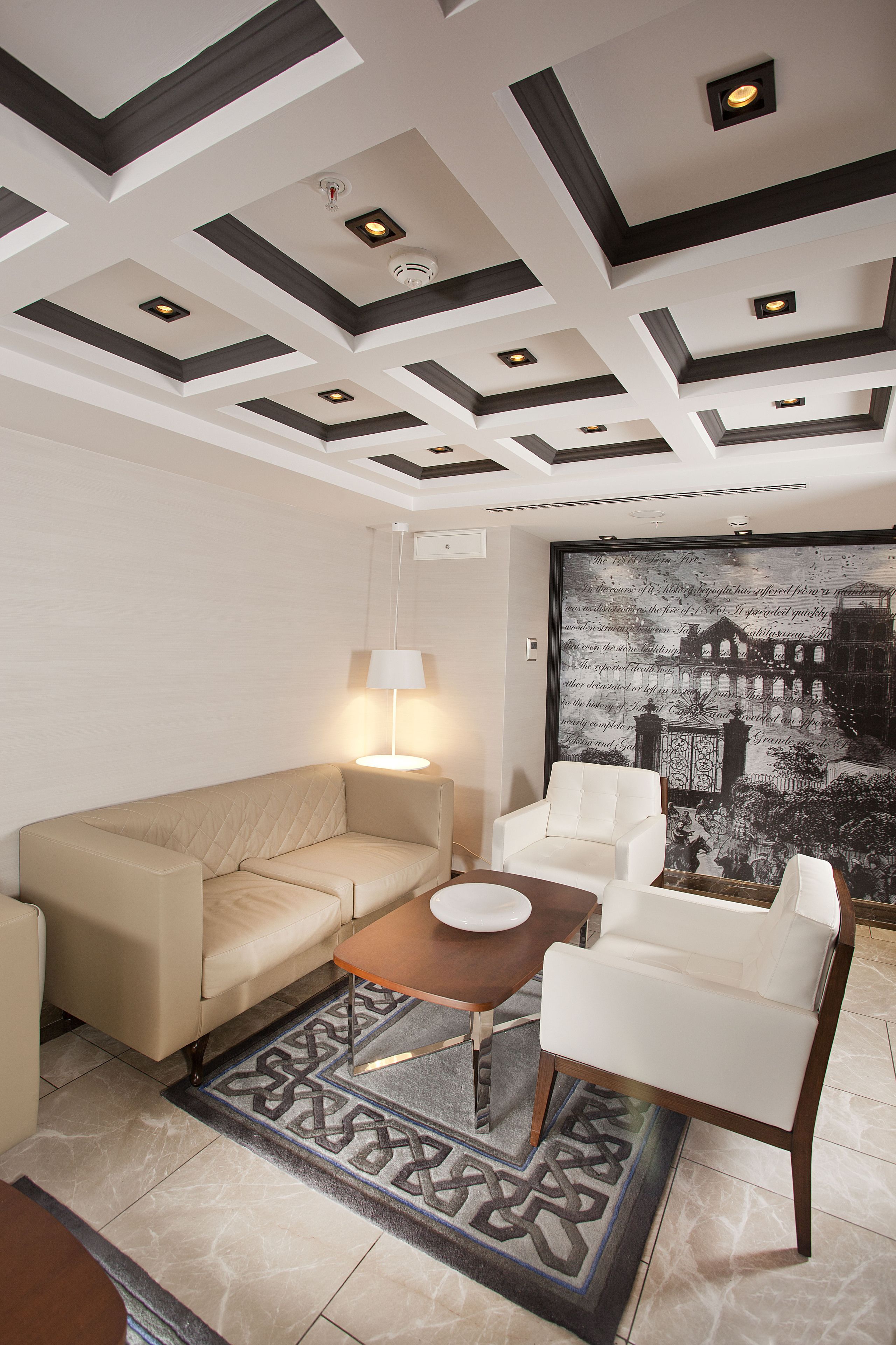 A modern living room with a beige sofa, white armchairs, a coffee table, and a patterned rug.