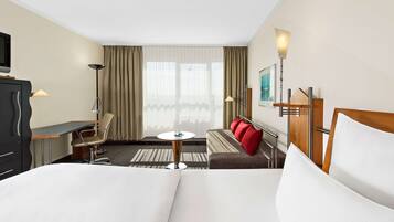 A hotel room with a bed, a desk, a chair, a small table, a sofa, and a TV.