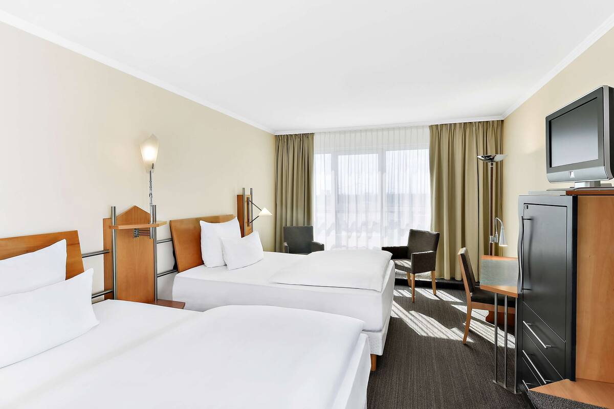 Ein Hotelzimmer mit zwei Betten, einem Schreibtisch, einem Sessel, einem Fernseher und einer Lampe.