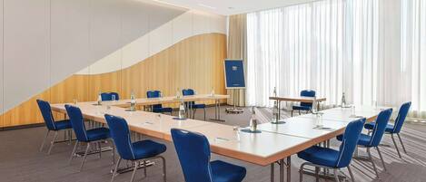 A conference room with a long table, blue chairs, and a large window with curtains.