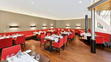 Un ristorante moderno con sedute e tavoli imbottiti rossi, pavimento in legno e illuminazione a incasso.