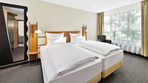A hotel room with a large bed, a bedside table, a mirror, and a window with curtains. - NH Mannheim-Viernheim (Viernheim)