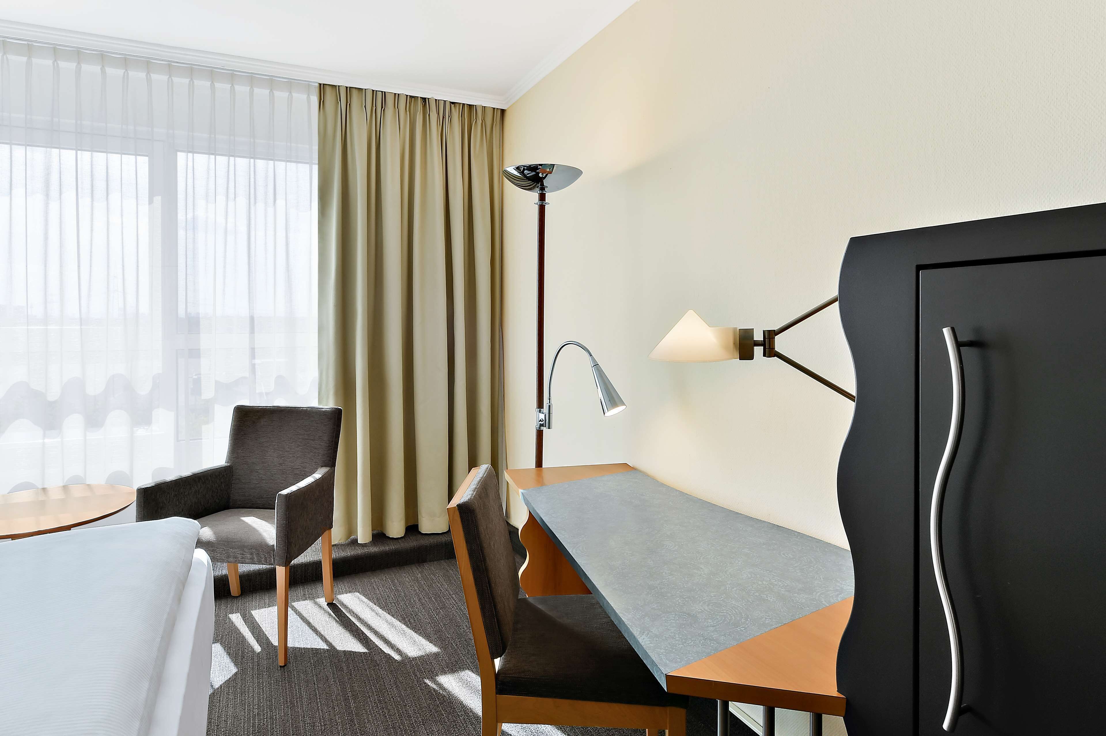 Ein Hotelzimmer mit einem Bett, zwei Stühlen, einem Schreibtisch, einer Lampe und einem Fernseher.